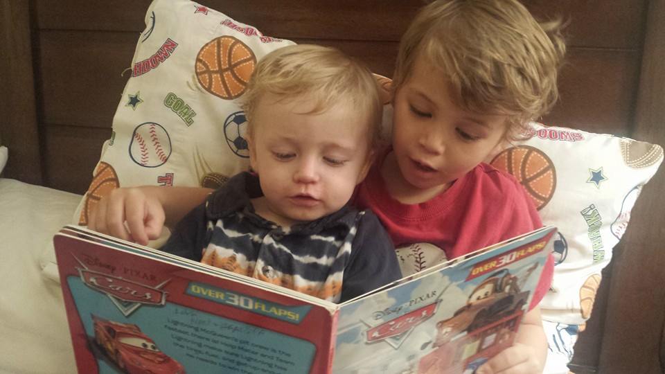 Two young boys read a book together in bed.