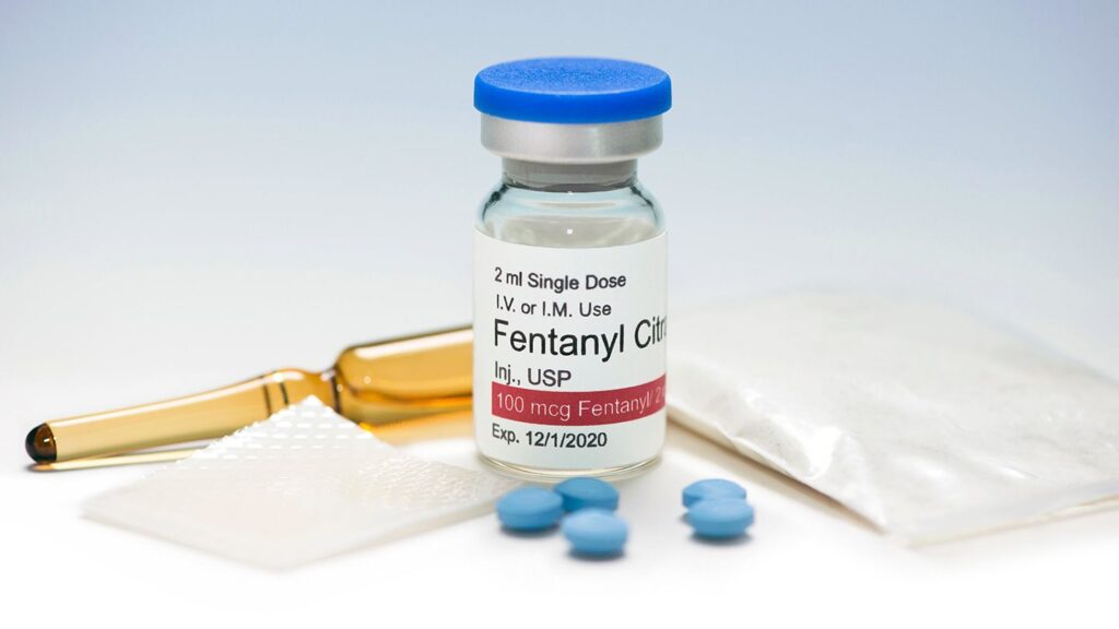 Image of a vial of liquid fentanyl, pills, and other drugs.