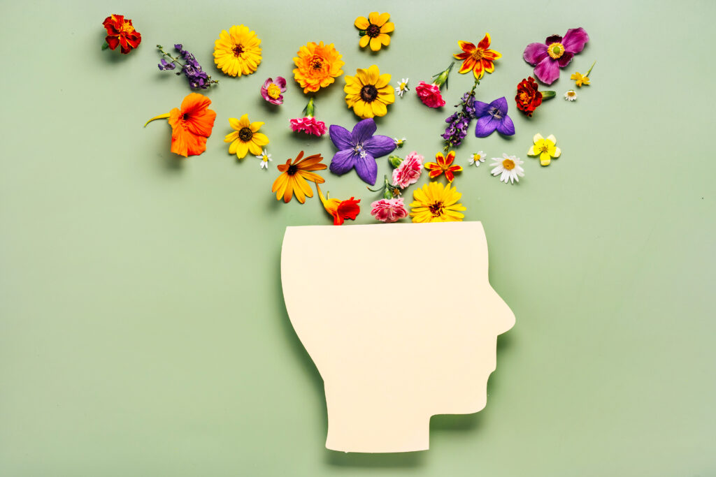 Mental health concept. Paper cut human head symbol and flowers on a green background