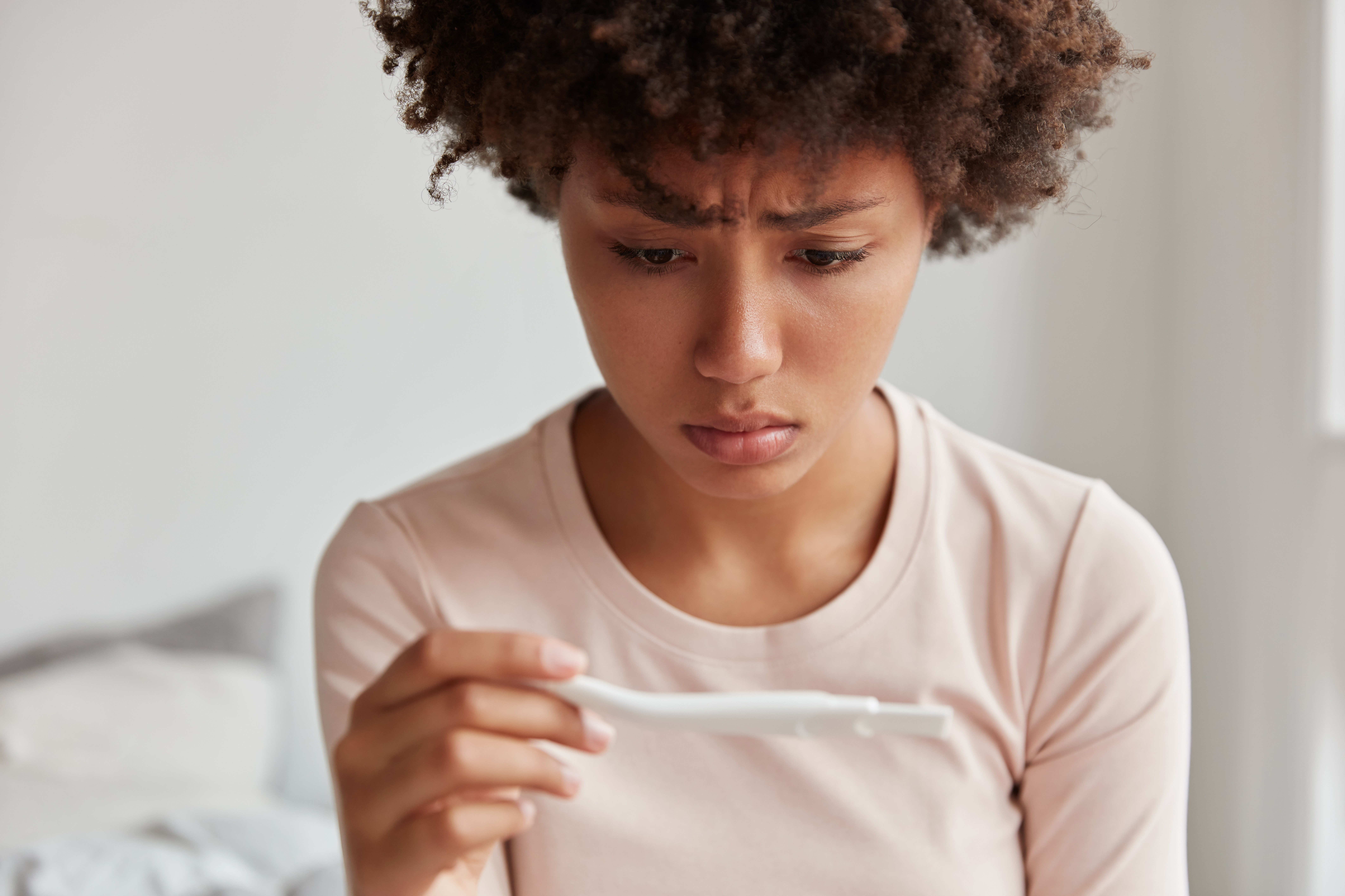 Unhappy black woman looks at pregnancy test