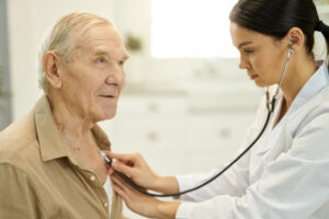 Focused professional doctor using stethoscope for examining a senior patient in front of her