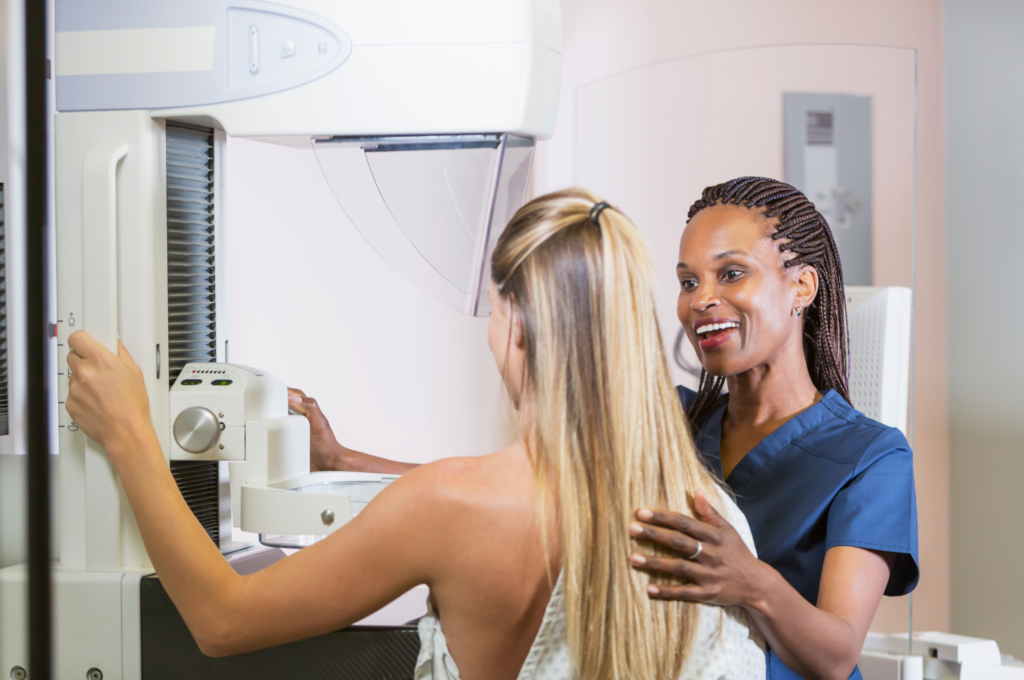 A young adult woman getting a mammogram. She is being helped by an African-American nurse.